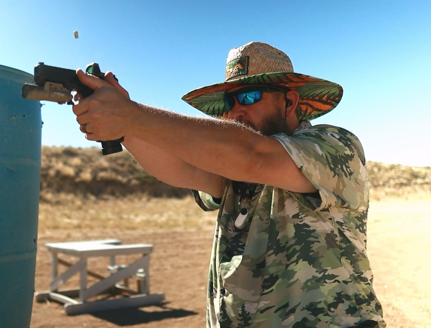 Shawn Herrin firing a handgun beside a blue barrel at an outdoor range